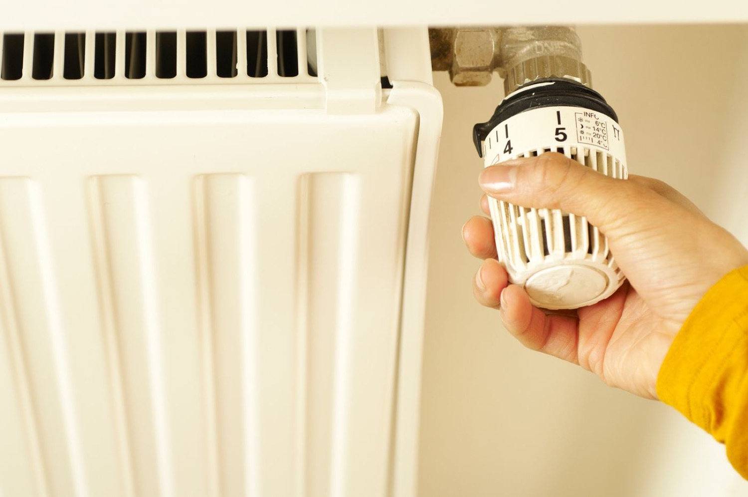 Main réglant un robinet thermostatique sur un radiateur blanc